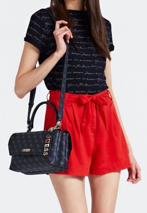 T-shirt noir avec un motif en écriture, associé à un short rouge taille haute. Sac à main bleu marine avec detail logo et finition texturée.