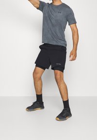 Camicia a maniche corte grigia a fantasia e pantaloni corti sportivi neri con logo Calvin Klein. Scarpe sportive nere con accenti grigi e suole in gomma.