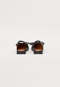 Sandalias de cuero negro con un diseño minimalista, que presentan una suela plana y correas traseras, caracterizadas por acentos de moño a los lados.