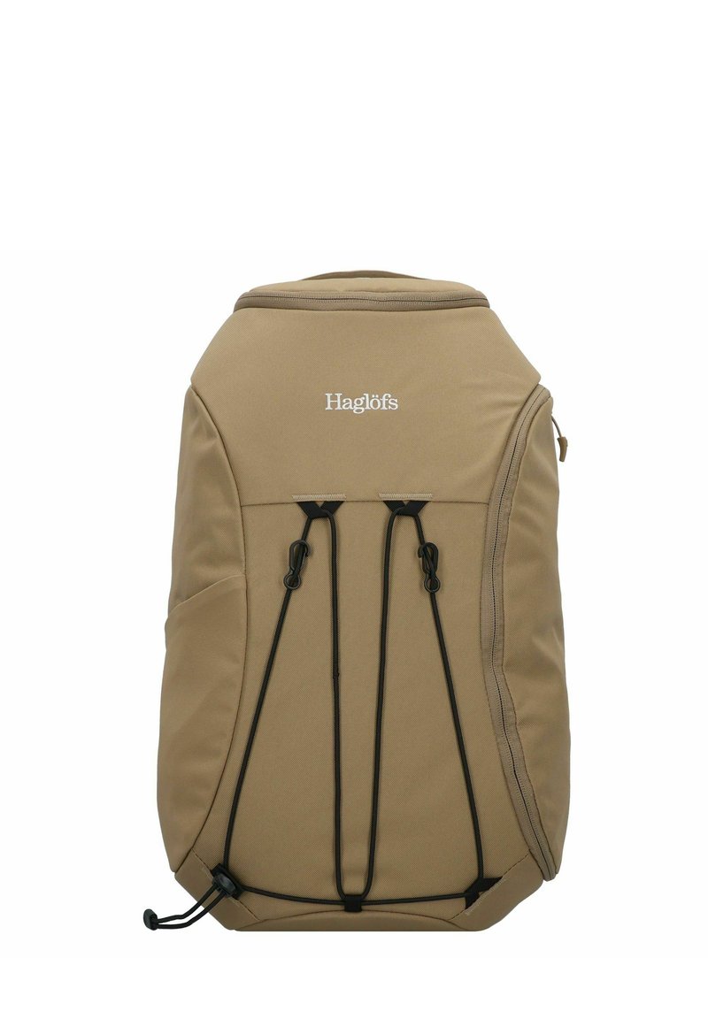 Sac à dos beige en tissu texturé, doté d'une fermeture éclair sur le dessus et de cordes bungee à l'avant pour un rangement supplémentaire. Logo affiché sur le devant.