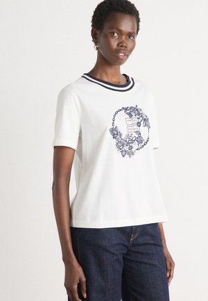 Witte katoenen T-shirt met marineblauwe gestreepte halslijn, korte mouwen en een bloemenafdruk aan de voorkant. Gecombineerd met donkerblauwe jeans.