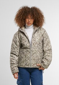 Kāmuflāžas raksta pūkains jakas, kas ir klusināti brūnā un pelēkā krāsā, ar rāvējslēdzēja fronti, lielu kapuci un elastīgām aprocēm. Strukturēta auduma, lai nodrošinātu siltumu.