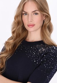 Pulover bleumarin cu mâneci scurte, având un corp tricotat texturat și decorat cu paiete împrăștiate în zona umerilor.