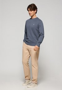 Blå bomullströja med rundad halsringning, ribbade ärmslut och nederkant. Beige bomullsnederdelar och vita sneakers fulländar outfiten.