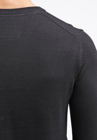 Czarny dzianinowy sweter z okrągłym dekoltem. Posiada bezszwowe ramiona, ściągacze na mankietach oraz gładką fakturę. Brak widocznych logo lub wzorów.