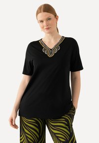 Sort kortærmet t-shirt med en dekorativ V-hals og intrikate perle- og broderidetaljer i sølv, sort og guld.