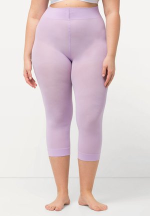 Frau trägt hoch taillierte, kurz geschnittene fliederfarbene Leggings und steht barfuß vor weißem Hintergrund, Hände entspannt an den Seiten.