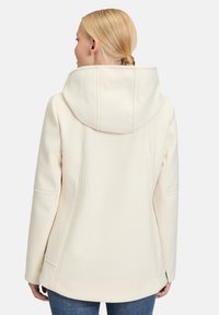 Cremefarvet hættetrøje med et blødt, tekstureret stof, der har sidelommer og sømdetaljer, vist fra ryggen.