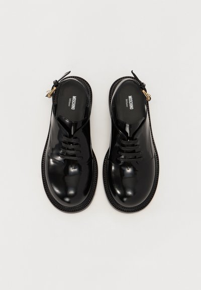 Black patent leather shoes with a rounded toe, lace-up design, and textured black sole. Features a gold hardware accent on the side.