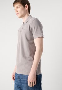 Šedá bavlněná polo košile s klasickým límečkem, zapínáním na dva knoflíky a krátkými rukávy. Na hrudi je jemně vyšitá značka.