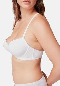 Soutien-gorge blanc avec des bretelles réglables, des bonnets lisses et un design sans couture. Fabriqué en tissu doux avec un détail de logo subtil sur le côté.