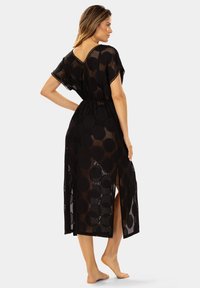 Czarny, przeźroczysty narzut z luźnym fasonem, krótkimi rękawami oraz okrągłymi wzorami. Posiada dekolt w kształcie litery V oraz boki z rozcięciami, co podkreśla swobodę ruchów.