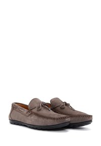 Mocasines de ante marrón con punta redonda, costuras decorativas y cordones en la parte delantera. Suela de goma negra para ofrecer agarre y flexibilidad.