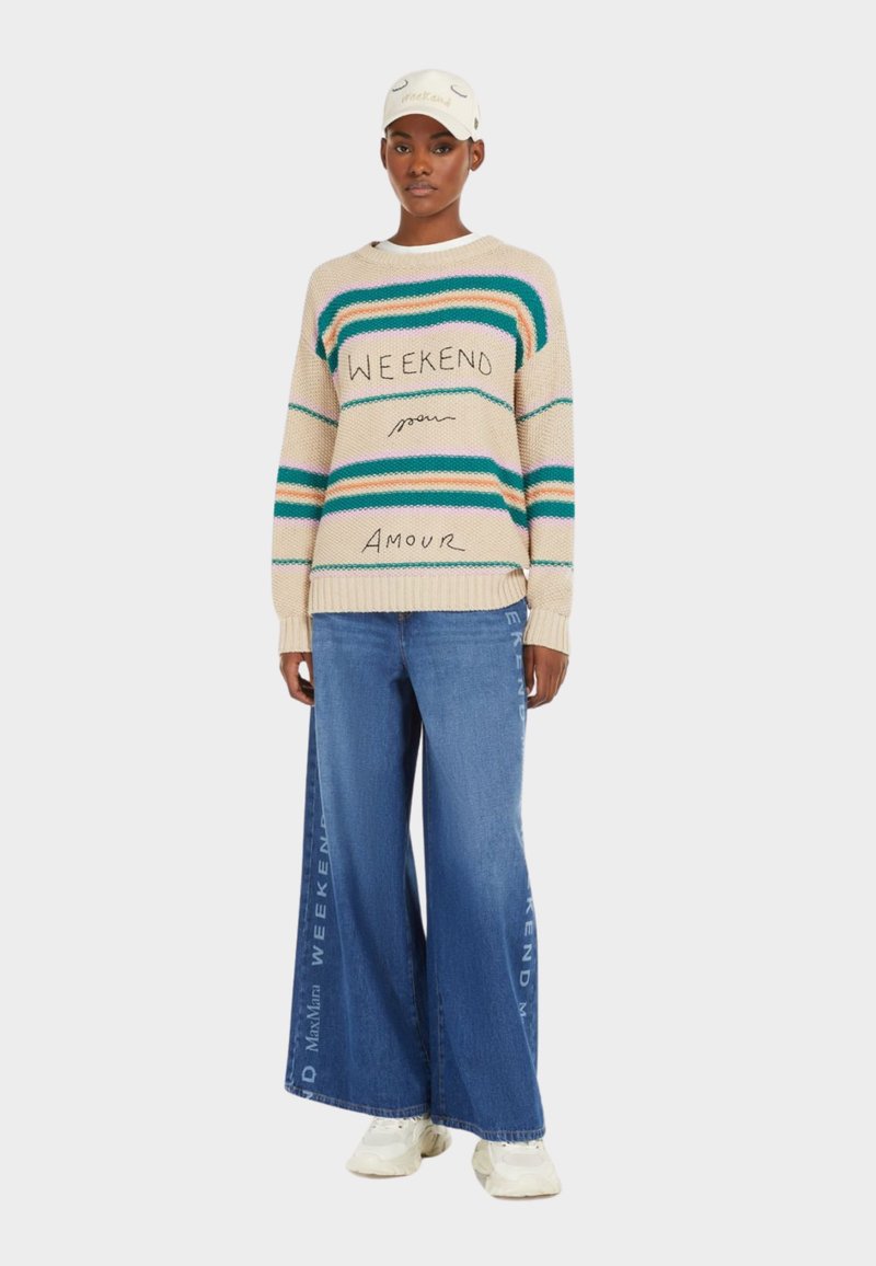 Knit sweater in beige with green and blue stripes, featuring "WEEKEND" text. Paired with wide-leg blue jeans and white sneakers.