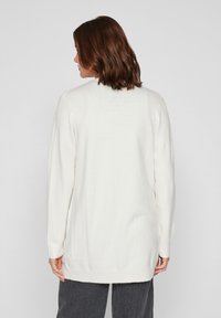 Suéter blanco de punto con mangas largas, dobladillo acanalado y corte relajado. Textura suave, con una abertura en la espalda para un detalle adicional.