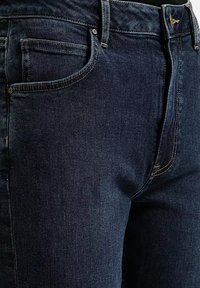 Granatowe dżinsy o klasycznym kroju, z pięcioma kieszeniami, kontrastowym przeszyciem oraz zapięciem na guzik i zamek.