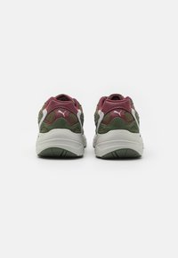 Zapatillas deportivas verdes y burdeos con materiales de malla y ante, cuello acolchado, acentos blancos y suela de goma texturizada.