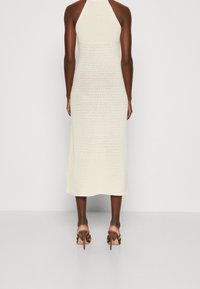 Robe midi en tricot de couleur crème clair, dotée d'un col halter et d'une texture côtelée. Associée à des talons marron à brides.