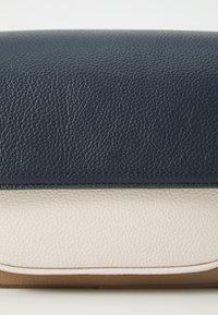 Läderhandväska i marinblått och kräm, med en texturerad yta, rektangulär form, kontrasterande färger och ljusbrunt kanting.