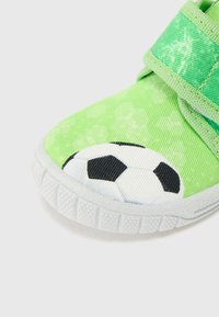 Grön textil sneaker med ett fotbollsgraphic, kardborreband och en texturerad vit gummisula för bra grepp.