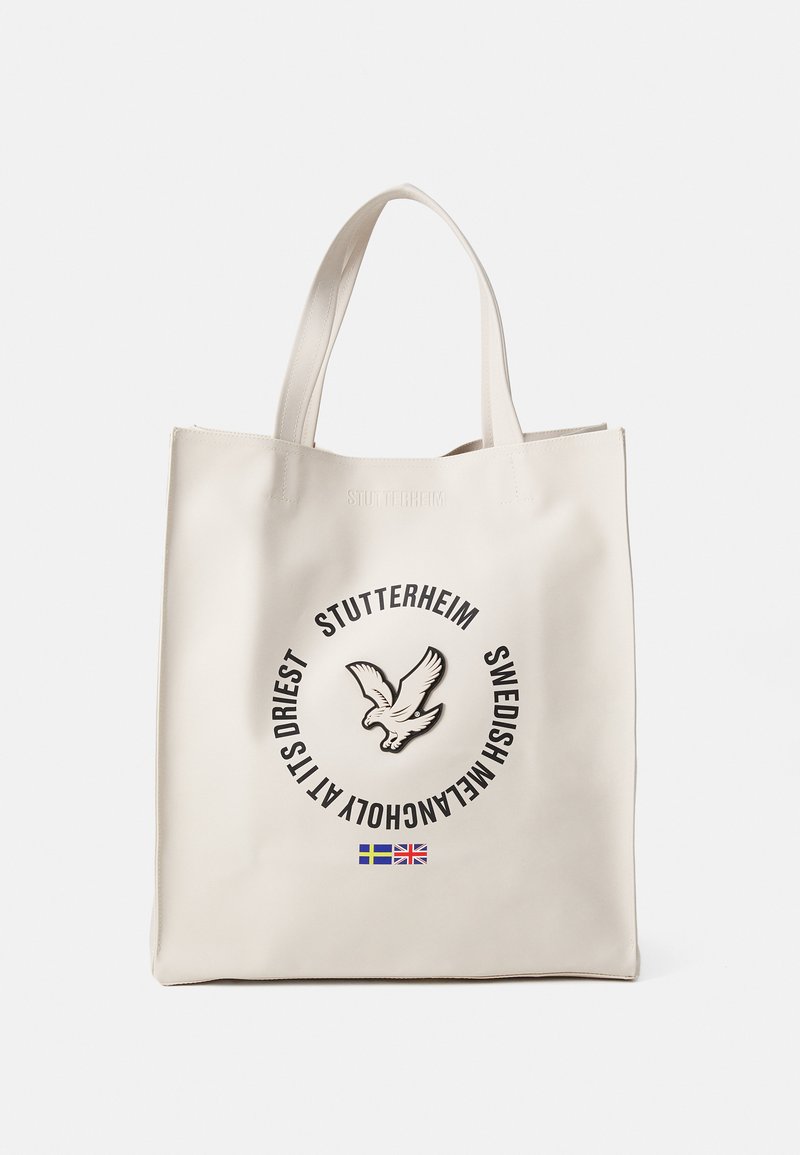 Kremowa torba na ramię wykonana ze skóry, z centralnym logo z grafiką ptaka i okrągłym tekstem. Podwójne uchwyty u góry.