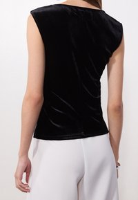 Top sin mangas de terciopelo negro con un diseño ajustado, que presenta un escote redondo y una textura suave, combinado con pantalones blancos de cintura alta.