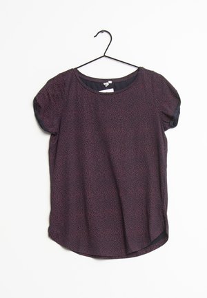 Blouse à manches courtes de couleur violet foncé avec un petit motif floral, encolure arrondie, suspendue à un cintre noir sur fond blanc.