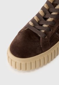 Baskets en suède marron avec une semelle en caoutchouc beige épaisse, présentant des lacets marron et des accents beige sur le dessus. Gros plan de la zone des orteils.
