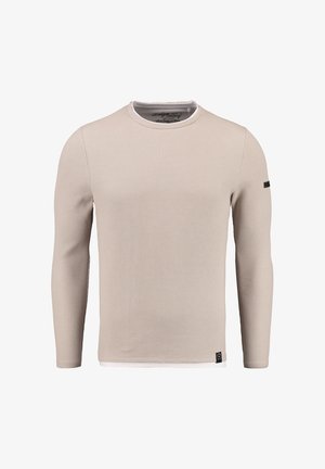 Chemise à manches longues beige clair avec texture côtelée, col rond, col intérieur blanc contrastant et étiquette noire sur la manche gauche.