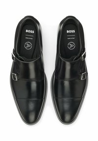 Schwarze Lederschuhe mit glänzendem Finish, ausgestattet mit doppelten Schnallendetails, rund zulaufender Spitze und strukturierter Innensohle. Hergestellt in Italien.