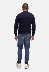 Maglione blu scuro, design aderente, polsini a coste; jeans azzurri chiari con tasche posteriori doppie e dettagli di cucitura; scarpe sportive grigie.