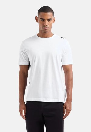 T-shirt blanc à manches courtes avec un col rond et des panneaux latéraux noirs, arborant un petit logo sur l'épaule. Texture en coton lisse.