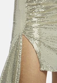 Minijupe argentée brillante avec une fente sur le côté, présentant une surface texturée de petites paillettes réfléchissantes et une silhouette épurée.