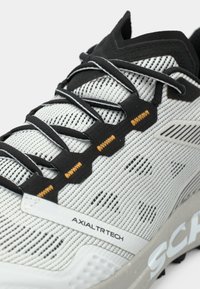 Leichtgewichtiger Sportschuh mit einem atmungsaktiven weißen Mesh-Obermaterial, schwarzen Akzenten und strukturierten Schnürsenkeln mit orangefarbenen Details.