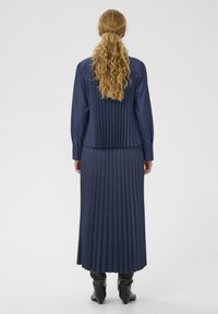 Granatowa sukienka plisowana z długimi rękawami i kołnierzykiem. Gładka tekstura, długość do kostek, zestawiona z czarnymi botkami za kolano.