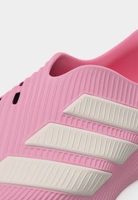 Rožinė įmaunama avalynė su faktūruotu paviršiumi ir trimis baltomis įstrižomis juostomis šone, matomas batelio kulnas ir viršutinė kraštinė.