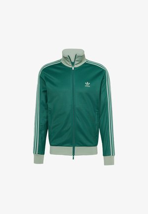 Jachetă verde cu fermoar, cu guler înalt, având trei dungi albe pe mâneci și un mic logo pe piept. Textură netedă.