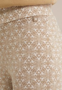 Bež legice s potiskom, ki vsebuje bel cvetlični vzorec, narejene iz mehke tkanine. Okrašene z majhno oznako z zvezdnatim detajlom.