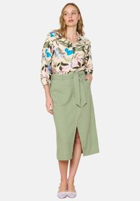 Blusa de estampado floral con flores azules y rosas, combinada con una falda de línea A en verde menta que cuenta con un lazo en la cintura y bolsillos laterales.