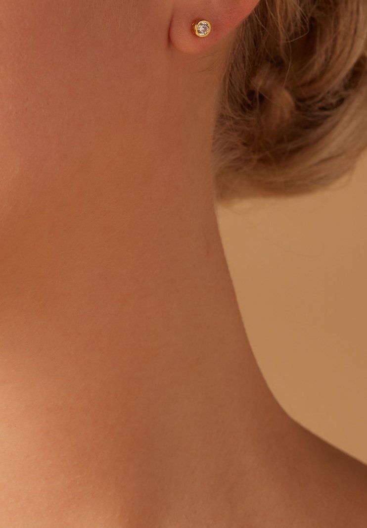 Boucle d'oreille en or avec une pierre précieuse claire au centre, sertie dans un chaton arrondi, mise en valeur sur un fond neutre.