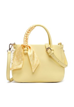 Bolso amarillo con asa trenzada envuelta en pañuelo amarillo con lunares, correa de hombro ajustable y accesorio de llavero blanco.