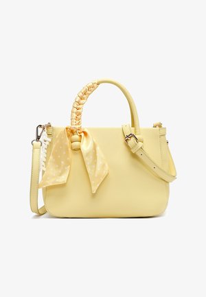 Bolso amarillo con asa trenzada envuelta en pañuelo amarillo con lunares, correa de hombro ajustable y accesorio de llavero blanco.