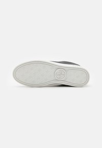 Sneaker nera con una tomaia testurizzata, suola di gomma bianca e battistrada a motivi. Presenta un logo sulla suola.