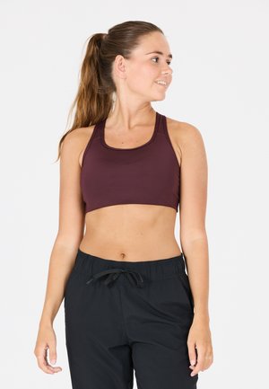 Vinröd sport-bh med justerbara axelband, slät textur och en figurnära design. I kombination med svarta shorts med dragsko.
