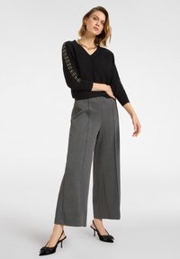 Czarny sweter w serek z fakturowaną boczną panelem, zestawiony z szarymi spodniami w szerokim kroju oraz czarnymi mule na obcasie z detalem w postaci kokardy.