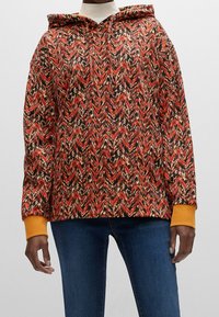 Sudadera con capucha que presenta un patrón en zigzag en rojo, negro y crema, con puños naranjas y un corte relajado. Fabricada en tejido suave.