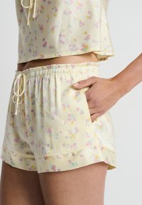 Conjunto de pijama floral amarillo que incluye una camiseta de manga corta y pantalones cortos a juego. El material tiene una textura suave y lisa, con una cinturilla elástica y cordón ajustable.