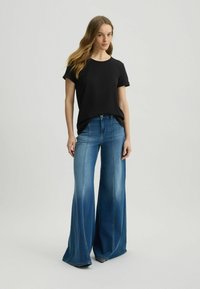 T-shirt nero a maniche corte abbinato a jeans blu a vita alta con gamba larga, caratterizzati da un lavaggio sbiadito e dettagli delle cuciture a contrasto.