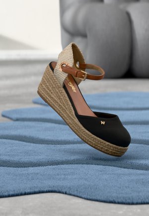 Kileespadrille med sort tå, flettet jutesål, beige ankelrem med spænde og lille gyldent "W"-detalje på tåen.