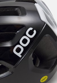 Primer plano de un casco de ciclismo en blanco y negro para personas de color, con orificios de ventilación y una etiqueta de seguridad Mips amarilla.